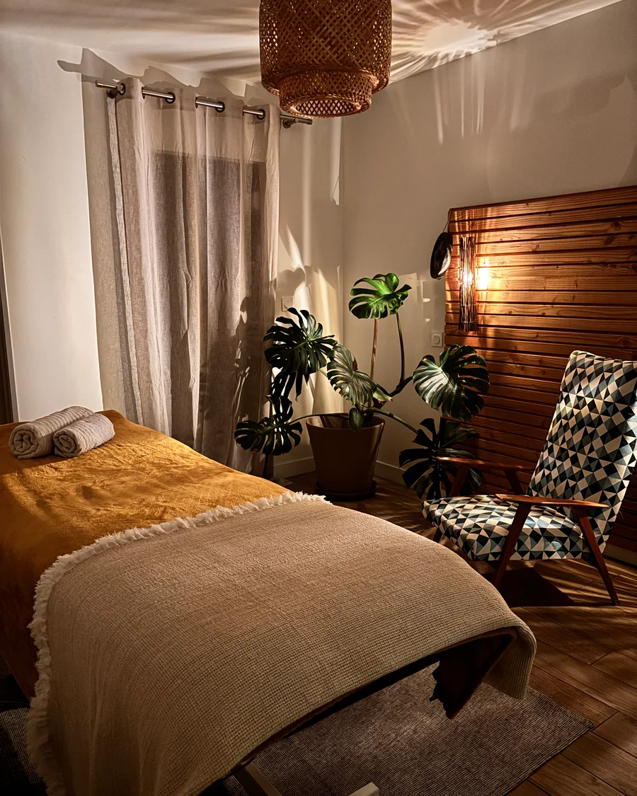 La table de massage préparée, serviettes roulées et monstera, dans la lumière chaude de la pièce
